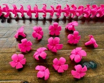 May include: Bright pink flower-shaped embellishments and a matching garland are scattered on a wooden surface. The flowers have five petals and are evenly spaced. The garland is a series of connected flower-like shapes. The overall theme is floral.