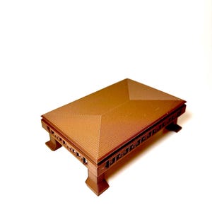 Puede incluir: Una mesa marrón en miniatura con un diseño geométrico. La mesa tiene una parte superior rectangular con una estructura inclinada en forma de techo y cortes decorativos en los lados. Se apoya sobre cuatro patas robustas.