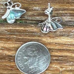 May include: A pair of silver butterfly earrings with iridescent abalone shell wings. The earrings are shown next to a US dime for size comparison.