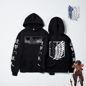 Op de afbeelding: Zwarte hoodie met anime-afbeeldingen. De voorkant toont een karakterafbeelding en Japanse tekst, de achterkant toont een wit en zwart vleugel-embleem. Japanse tekst is ook op de mouwen gedrukt.