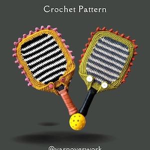 Könnte beinhalten: Zwei gestrickte, gestreifte Pickleball-Schlägerbezüge in Gelb, Orange, Rosa, Grün und Grau mit schwarzen Streifen. Die Bezüge sind an den Schlägern befestigt und ein gelber Pickleball befindet sich dazwischen. Der Text "@yarnoverwork" befindet sich am unteren Rand des Bildes.