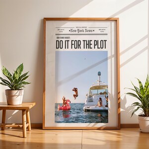 Può includere: Una stampa incorniciata con il titolo "DO IT FOR THE PLOT" in stile giornale. L'immagine mostra persone che saltano in mare da una barca e un gommone rosa. La stampa è in una cornice di legno, in un ambiente luminoso e soleggiato.