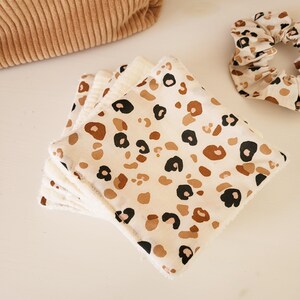 May include: A stack of white reusable makeup remover pads with a brown and black leopard print design.