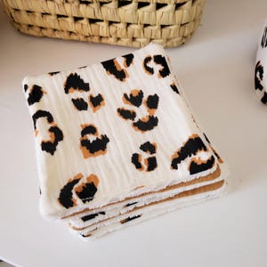 May include: A stack of white cotton washcloths with a brown and black leopard print. The washcloths have a brown terrycloth backing.