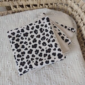 May include: A stack of three square baby washcloths. The top washcloth features a cream background with brown leopard spots. The other washcloths are a solid cream color. The washcloths are folded and stacked on top of each other.