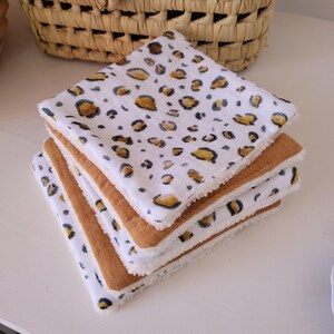 May include: A stack of four white cotton washcloths with a brown and yellow leopard print. The washcloths have a brown fleece backing.