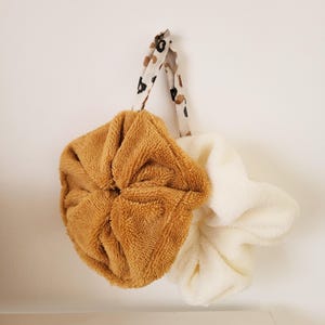 May include: Two fuzzy hair scrunchies, one brown and one white, with a leopard print fabric strap.
