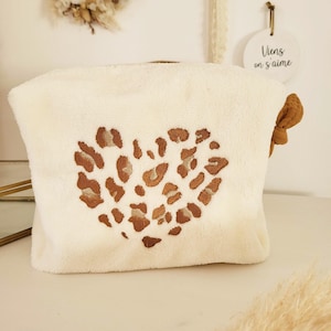 May include: A white, fuzzy makeup bag with a brown leopard print heart design. The bag has a brown fabric tie closure.