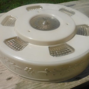 May include: A white ceiling light fitting with a floral design and six clear glass panels. The light fitting has a central dome with a decorative pattern.
