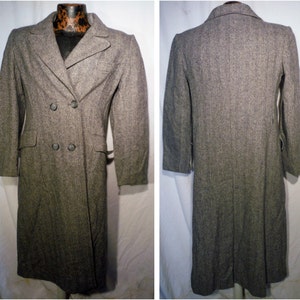 May include: A long, grey double-breasted coat with a herringbone pattern. The coat has a belt and two large buttons.