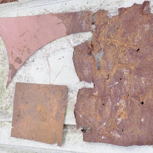 May include: Three distinct pieces of metal: one triangular segment with a smooth reddish-brown finish, one square piece with a weathered brown rusted surface, and one large, irregularly shaped sheet of heavily corroded, dark brown metal.