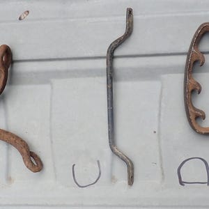 Op de afbeelding: Vijf verschillende metalen voorwerpen, gelabeld van A tot en met E. De voorwerpen zijn roestig en lijken antiek te zijn. Ze zijn in een rij op een lichtgrijs oppervlak gerangschikt.