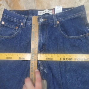 May include: Blue denim jeans with a wooden ruler measuring the waist. The ruler shows measurements in inches.
