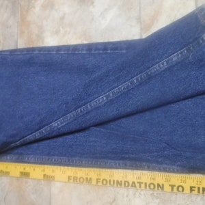 May include: A pair of blue denim jeans folded in half, with a yellow measuring tape placed along the bottom edge. The tape reads "From Foundation to Finish" and has markings in inches.