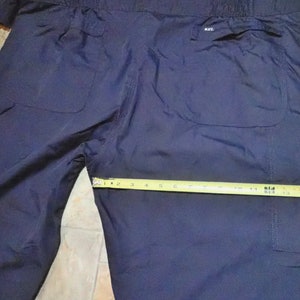 May include: Dark blue nylon pants with two large pockets on the back. The pants have a drawstring waistband and a label that says "K-II" on the right back pocket.
