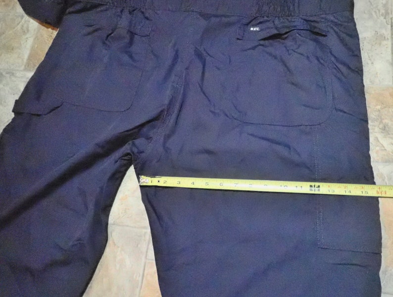 May include: Dark blue nylon pants with two large pockets on the back. The pants have a drawstring waistband and a label that says "K-II" on the right back pocket.