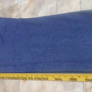 May include: A pair of blue denim jeans laid flat. The jeans have a single back pocket and a yellow measuring tape is placed below the jeans.
