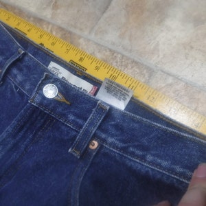 May include: A close-up of the waistband of a pair of blue denim jeans. The jeans have a button fly and a Levi's brand label.