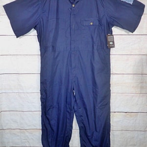 May include: A navy blue short-sleeved jumpsuit with a button-up front and a single chest pocket. The jumpsuit has a brand label that reads "KAVU" on the left side of the chest.