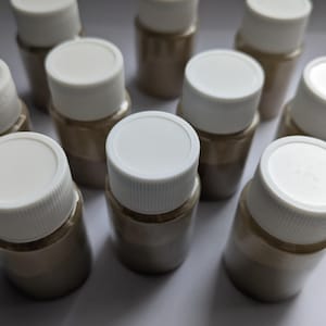 May include: Ten small, round, white plastic containers with brown powder inside. The containers have a screw-on lid.