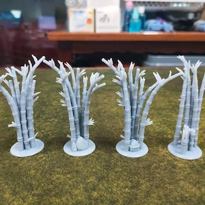 May include: Four miniature light blue bamboo plants with detailed trunks and branches. Each plant is mounted on a circular base. The plants are arranged in a row on a green surface.
