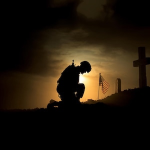 May include: Silhouette of a soldier kneeling in prayer in front of a grave marked with a cross and an American flag. The scene is set against a dark sky with a bright orange sunset in the background.
