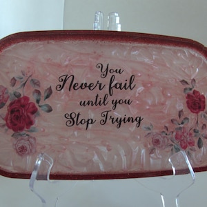 Op de afbeelding: Een rechthoekig decoratief dienblad met een rode glitterrand en een roze en witte marmeren achtergrond. De lade heeft bloemaccenten en de tekst "You Never fail until you Stop Trying" in zwart schrift.
