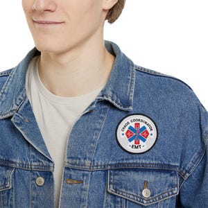 Könnte beinhalten: Eine blaue Jeansjacke mit einem weißen Patch, auf dem "Chaos Coordinator - EMT" mit einem roten und blauen Lebensstern-Symbol steht.