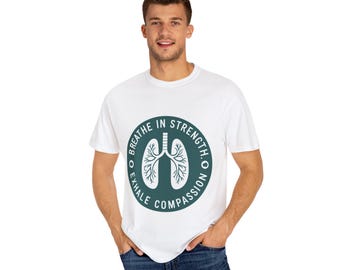 May include: White t-shirt with a circular teal graphic featuring a lung illustration and the words "Breathe in Strength. Exhale Compassion." The shirt is made of a soft material and has a crew neck.