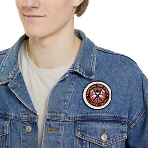 May include: A blue denim jacket with a red, white and black embroidered patch that says "Risking Our Ours To Save Yours".