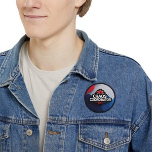 Puede incluir: Una chaqueta vaquera azul con un parche redondo que dice "Chaos Coordinator - EMT" en texto blanco. El parche tiene un diseño de estrella roja y azul.