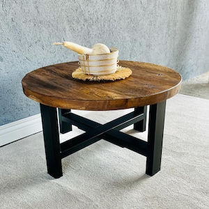 Op de afbeelding: Een ronde houten salontafel met een zwart metalen onderstel. De tafel heeft een natuurlijke houten afwerking en een kruisvormig ontwerp op het onderstel.