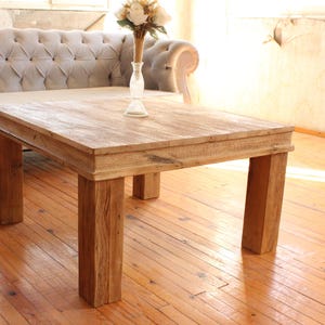 Könnte beinhalten: Rechteckiger Couchtisch aus Holz mit natürlicher Oberfläche. Der Tisch hat eine dicke Platte und vier stabile Beine. Eine Vase mit Blumen steht auf dem Tisch. Der Tisch ist etwa 100 cm lang.