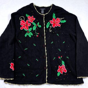 May include: Black cardigan sweater with red poinsettias, green leaves, and small red berries embroidered on the front. The sweater has a cream-colored trim and buttons. A festive holiday garment.