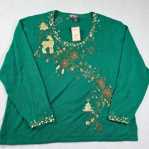 Könnte beinhalten: Ein grüner Langarmpullover mit goldenen Pailletten und Perlenverzierungen. Das Design umfasst ein Rentier, Weihnachtsbäume und florale Muster. Der Pullover hat einen runden Ausschnitt und ein Etikett.