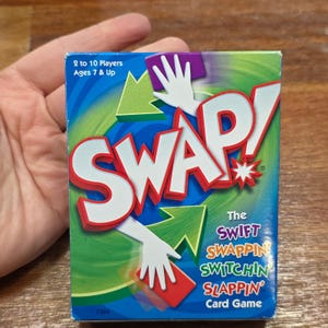 May include: A card game box with a blue background and the word "SWAP!" in large red letters. The box features the text "The SWIFT SWAPPIN SWITCHIN SLAPPIN Card Game" and indicates it's for 2 to 10 players, ages 7 and up.