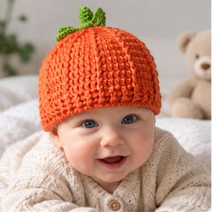 Peut inclure: Un bonnet au crochet orange vif conçu pour ressembler à une citrouille, présentant une texture côtelée verticale et un petit détail de tige et de feuille vertes au crochet fixé au centre supérieur de la calotte, en fil épais.