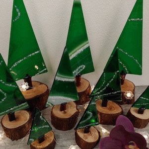 Puede incluir: Una colección de árboles de Navidad de vidrio verde con remolinos blancos, cada uno sobre una base de madera. Los árboles están dispuestos sobre una superficie de madera con una orquídea morada en primer plano.