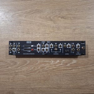 May include: A black Axis Modular Tool Belt synthesizer module featuring a twin slider attenuator with white and red sliders, multiple input and output jacks, an A/B switch, a clipper section, and an FX bypass toggle switch with white text labels.