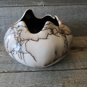 May include: A white ceramic bowl with black crackle glaze. The bowl has a unique, organic shape and is perfect for displaying flowers or other decorative items.