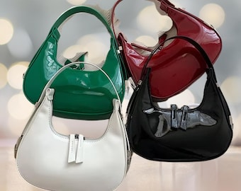 Puede incluir: Cuatro bolsos de mano brillantes de diferentes colores. Los bolsos tienen todos la misma forma, pero de diferentes colores: blanco, verde, rojo y negro.