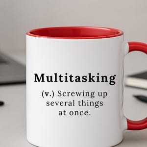 Puede incluir: Taza de cerámica blanca con interior y asa rojos. La taza presenta la palabra "Multitasking" en negro, seguida de una definición humorística: "(v.) Joder varias cosas a la vez."