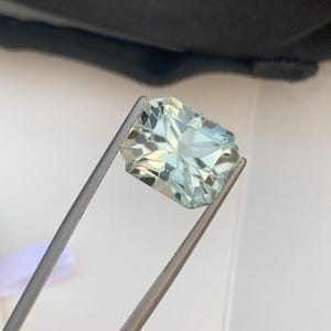 Peut inclure: Une pierre pr&eacute;cieuse rectangulaire bleu clair, tenue par une pince argent&eacute;e. La gemme est taill&eacute;e &agrave; facettes, refl&eacute;tant la lumi&egrave;re et r&eacute;v&eacute;lant sa structure interne. La couleur de la gemme est un bleu clair translucide.