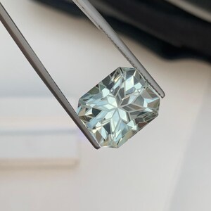 Peut inclure: Une pierre pr&eacute;cieuse rectangulaire bleu clair tenue par une pince. La gemme pr&eacute;sente un motif d'&eacute;clat d'&eacute;toile de facettes, refl&eacute;tant la lumi&egrave;re. La couleur de la pierre est vert d'eau p&acirc;le. La pince est argent&eacute;e et maintient la gemme en toute s&eacute;curit&eacute;.