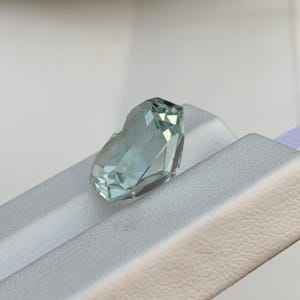 Peut inclure: Une pierre pr&eacute;cieuse bleu clair taill&eacute;e &agrave; facettes. La gemme pr&eacute;sente de multiples facettes qui r&eacute;fl&eacute;chissent la lumi&egrave;re, cr&eacute;ant un effet scintillant. La pierre est pos&eacute;e sur un fond blanc. Environ 2 cm de long.