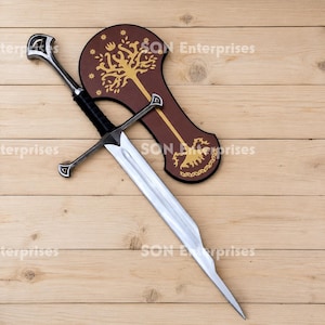 May include: A silver-coloured metal sword with a black wrapped handle and a crossguard, positioned diagonally over a brown shield-shaped plaque. The plaque features a gold-coloured graphic of a tree with stars and intricate root patterns.