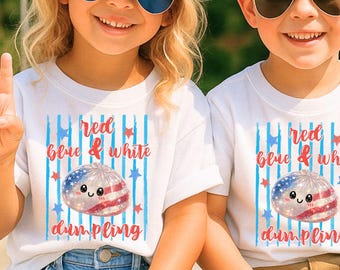May include: Two children wearing sunglasses and white t-shirts with a patriotic dumpling graphic and the text "Red, Blue & White Dumpling." One child wears a blue cap with a white star. The American flag is in the background.