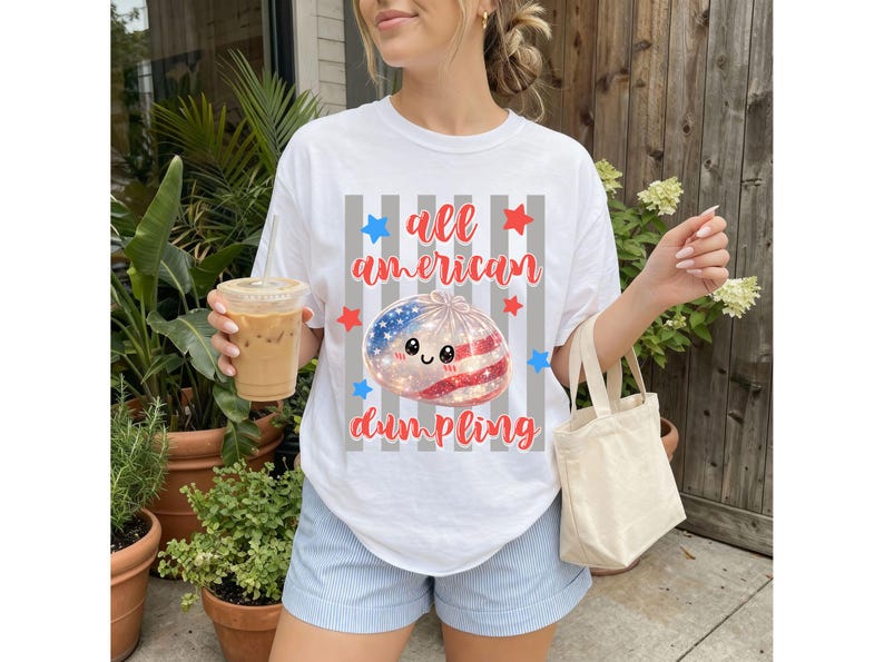 May include: White t-shirt with the text "all american dumpling" in red script. The graphic features a dumpling with an American flag design, surrounded by red and blue stars. The shirt is worn with blue shorts.