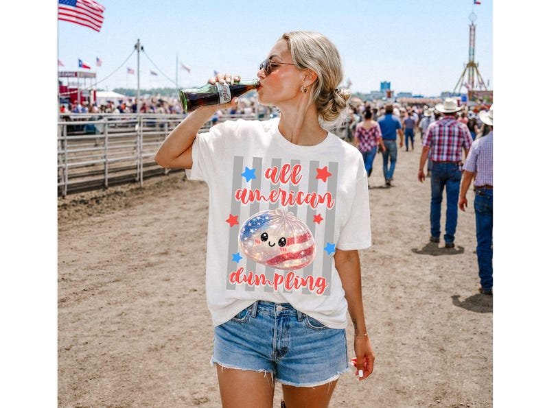 May include: White t-shirt with the text "all american dumpling" and a graphic of a dumpling with an American flag design. The shirt is paired with denim shorts. A person is drinking from a Coca-Cola bottle.