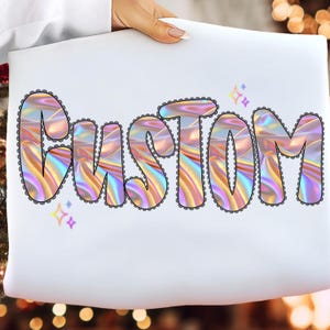 May include: A white surface displays the word "CUSTOM" in large, holographic letters. The letters have a wavy, iridescent design with a black scalloped border. Small, purple star shapes are scattered around the word.